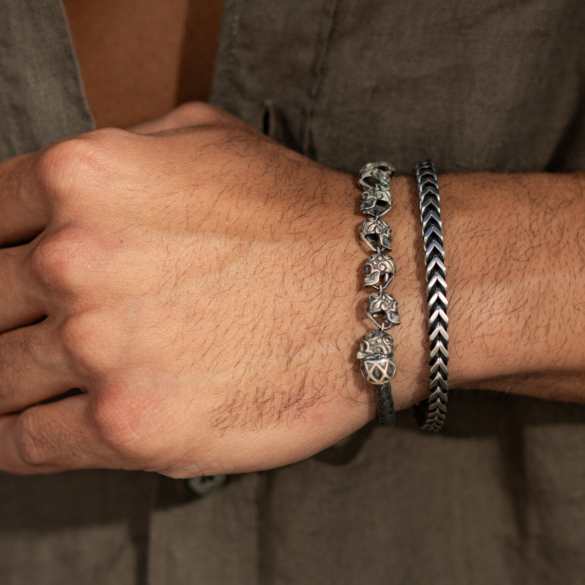 Close view of the engraved skull links on a man's wrist, stacked with a black and silver chevron bracelet