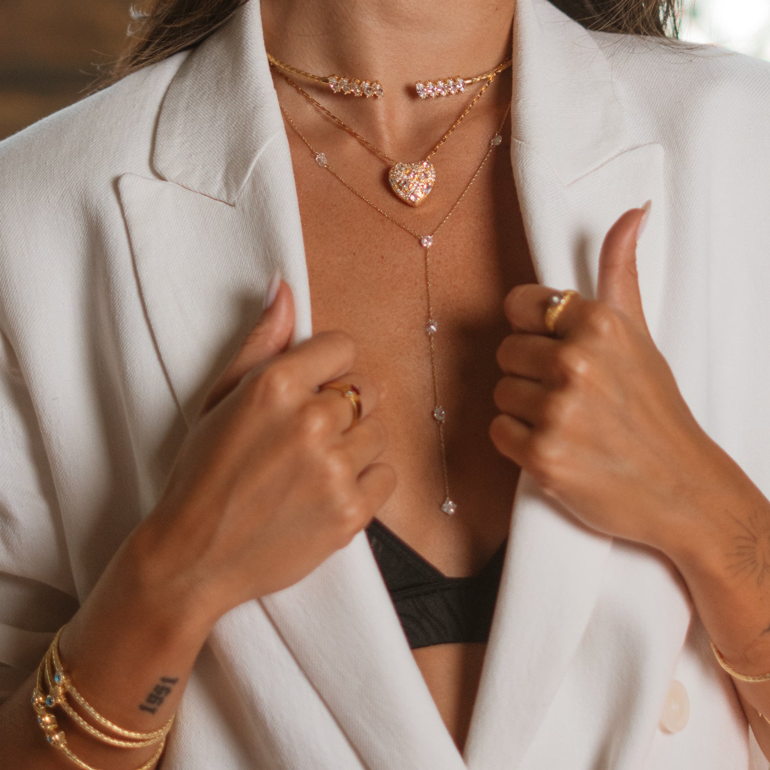 Close up of a gold mosaic heart pendant layered with delicate gold chains over a white blazer