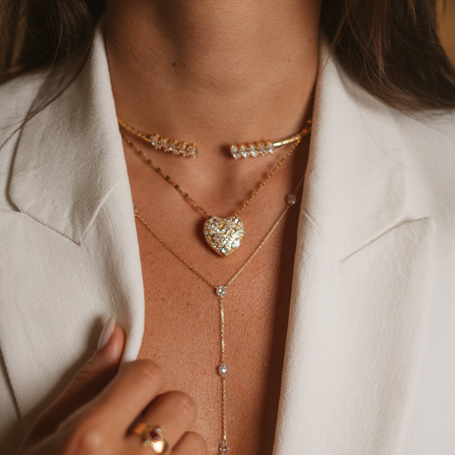Woman in a white blazer wearing a sparkly gold heart necklace layered with fine gold chains