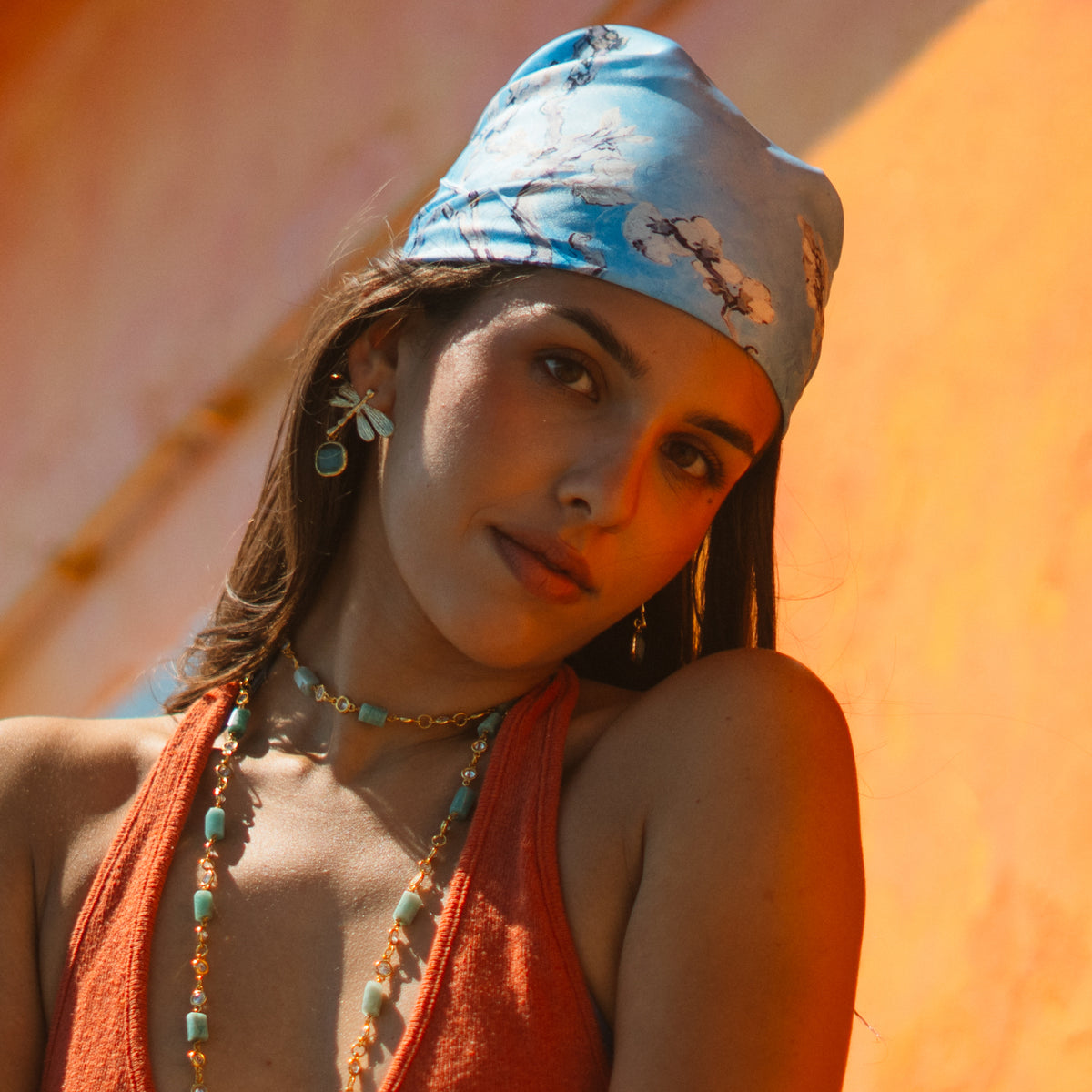 Portrait of a model in a blue headscarf wearing the Spiritual Dragonfly aqua blue cat's eye gold drop earring