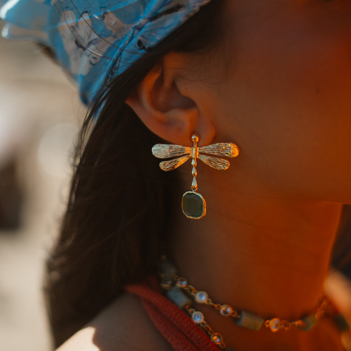 Close side view of the Spiritual Dragonfly earring on the ear, the aqua cat's eye stone hanging below the gold wings