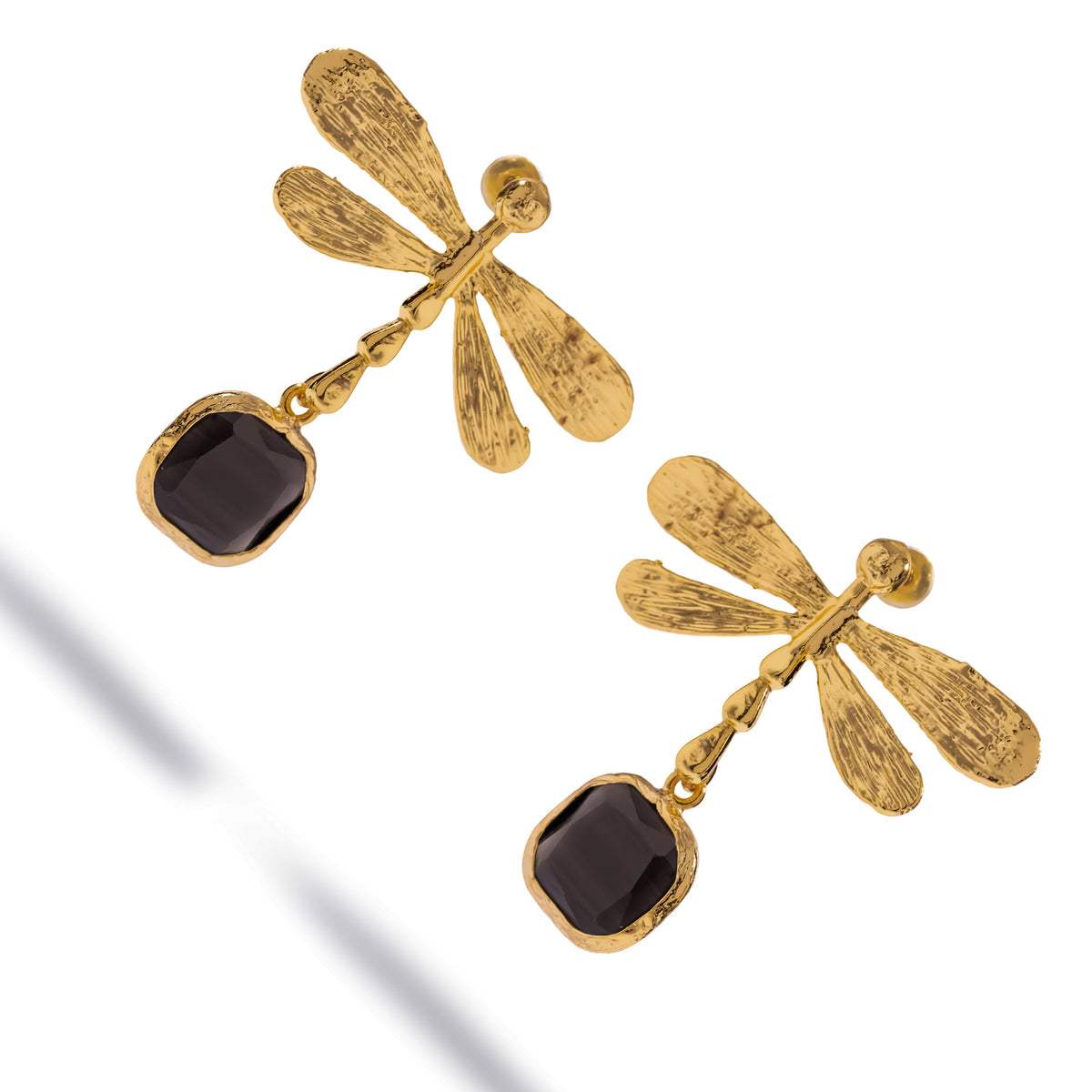 Angled studio view of the gold dragonfly earrings showing the textured wings, segmented body and black cat's eye stones