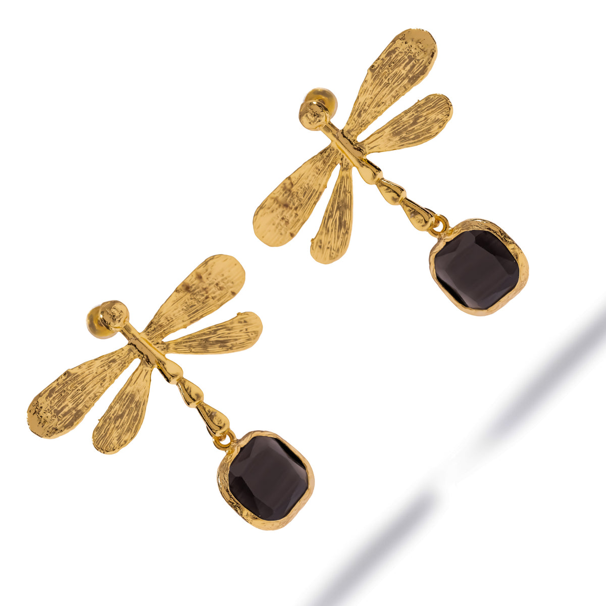 Overhead studio view of the Spiritual Dragonfly earrings, the black cat's eye stones framed in textured gold bezels