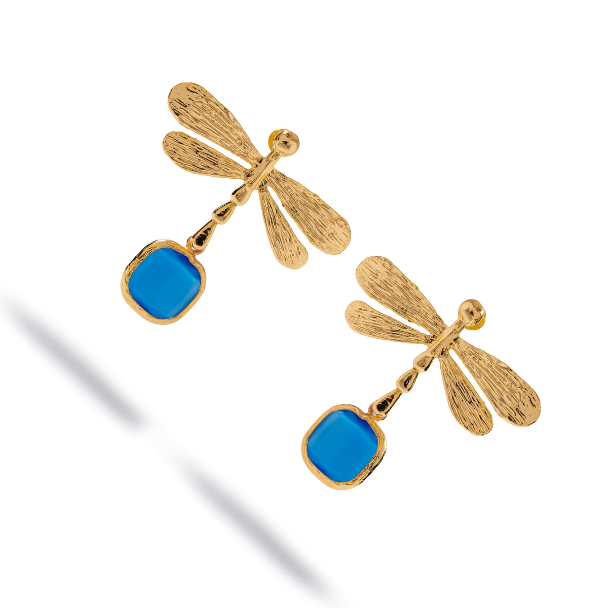 Angled studio view of the gold dragonfly drop earrings, the deep blue cat's eye stones set in textured gold bezels