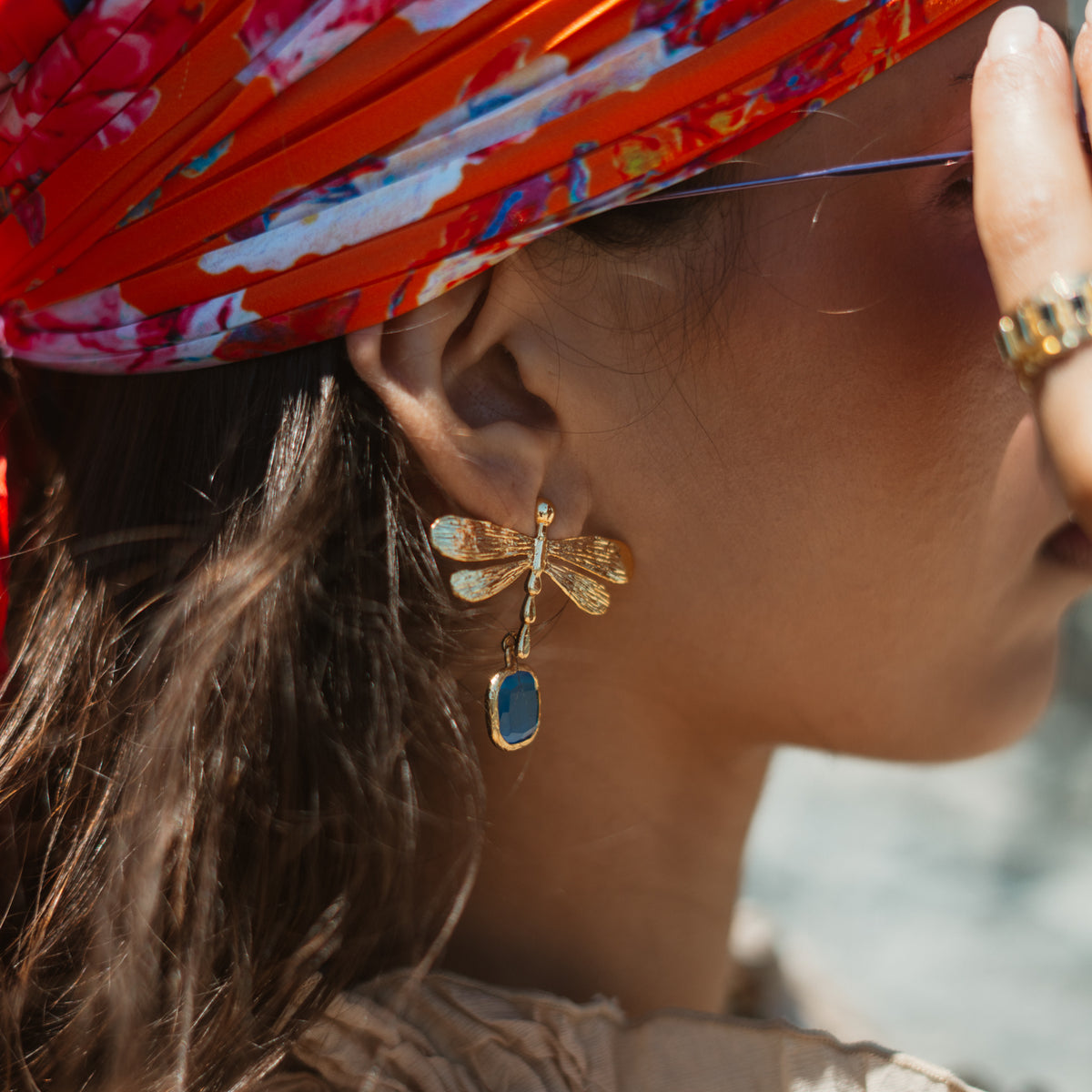 Close view of the gold dragonfly earring with its blue cat's eye drop, worn under a red and blue silk headscarf