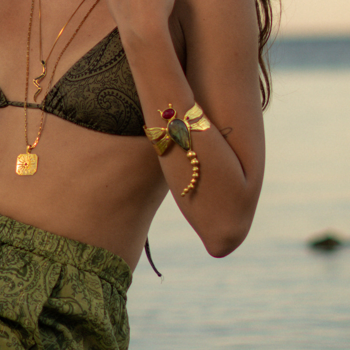 Woman by the sea wearing the Spiritual Dragonfly Labradorite & Ruby Gold Cuff Bracelet on her upper arm