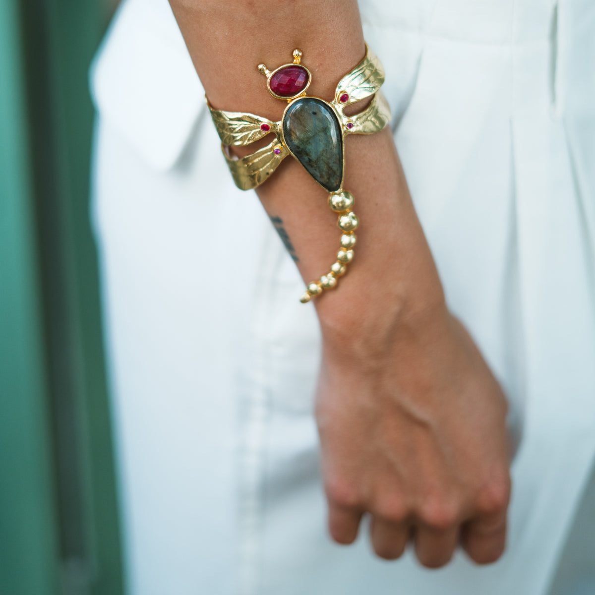 Spiritual Dragonfly Labradorite & Ruby Gold Cuff Bracelet worn on the wrist over white tailoring
