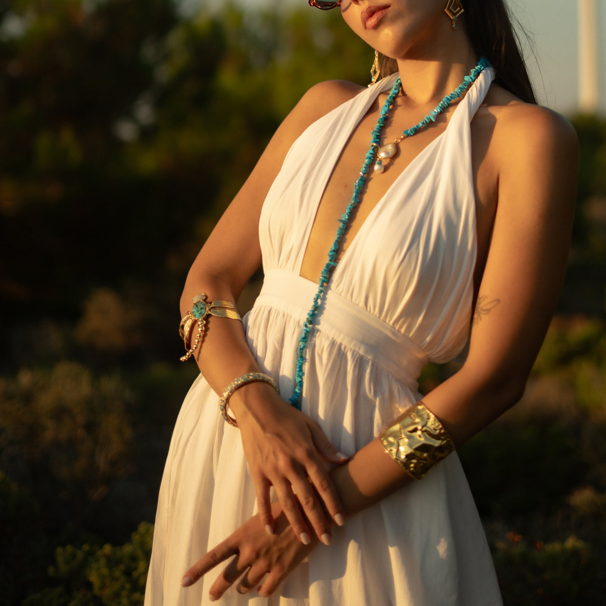 Model in a white dress wearing the Spiritual Dragonfly Turquoise & Ruby Gold Cuff Bracelet with a long turquoise necklace