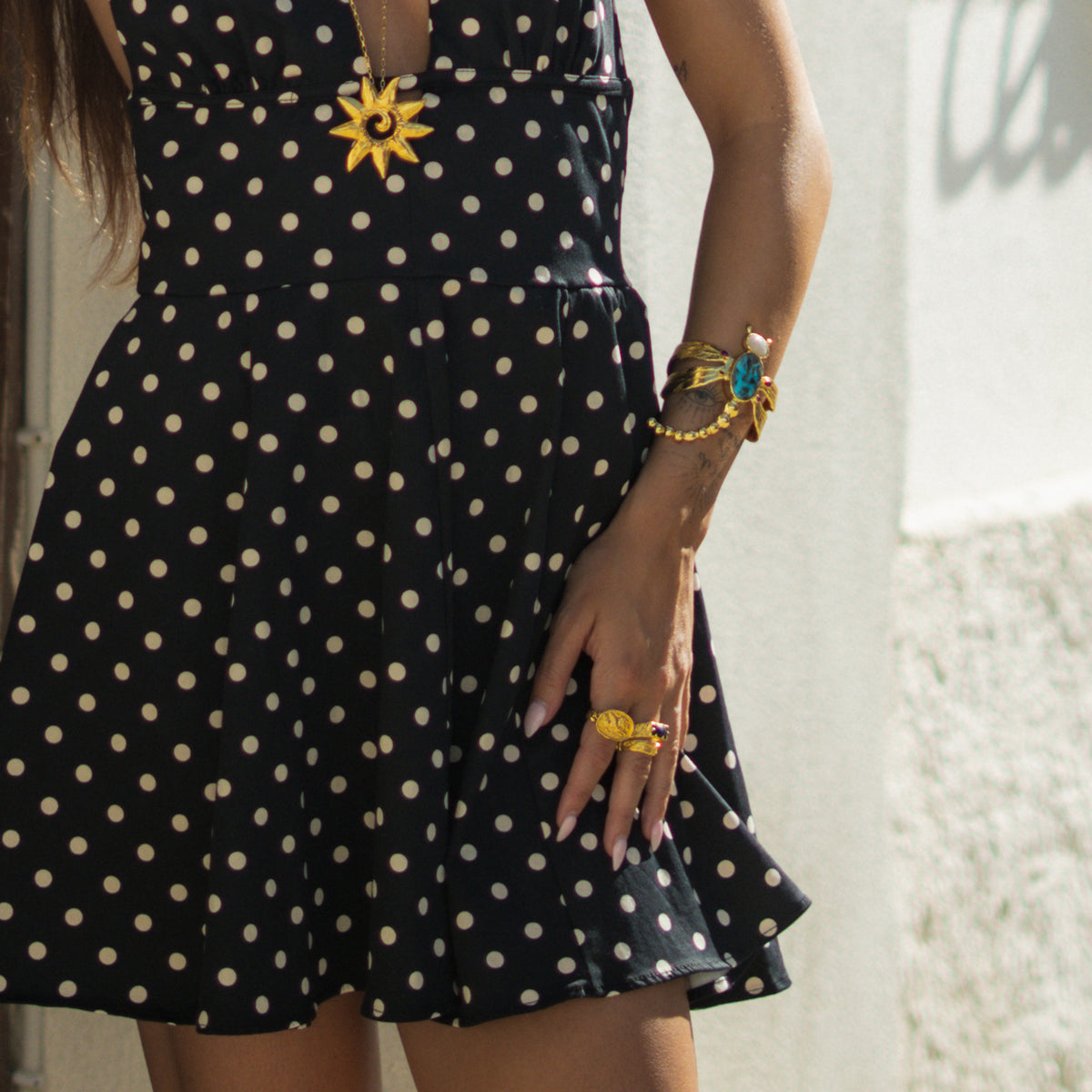 Woman in a polka dot dress wearing the turquoise dragonfly gold cuff with a gold sun pendant necklace