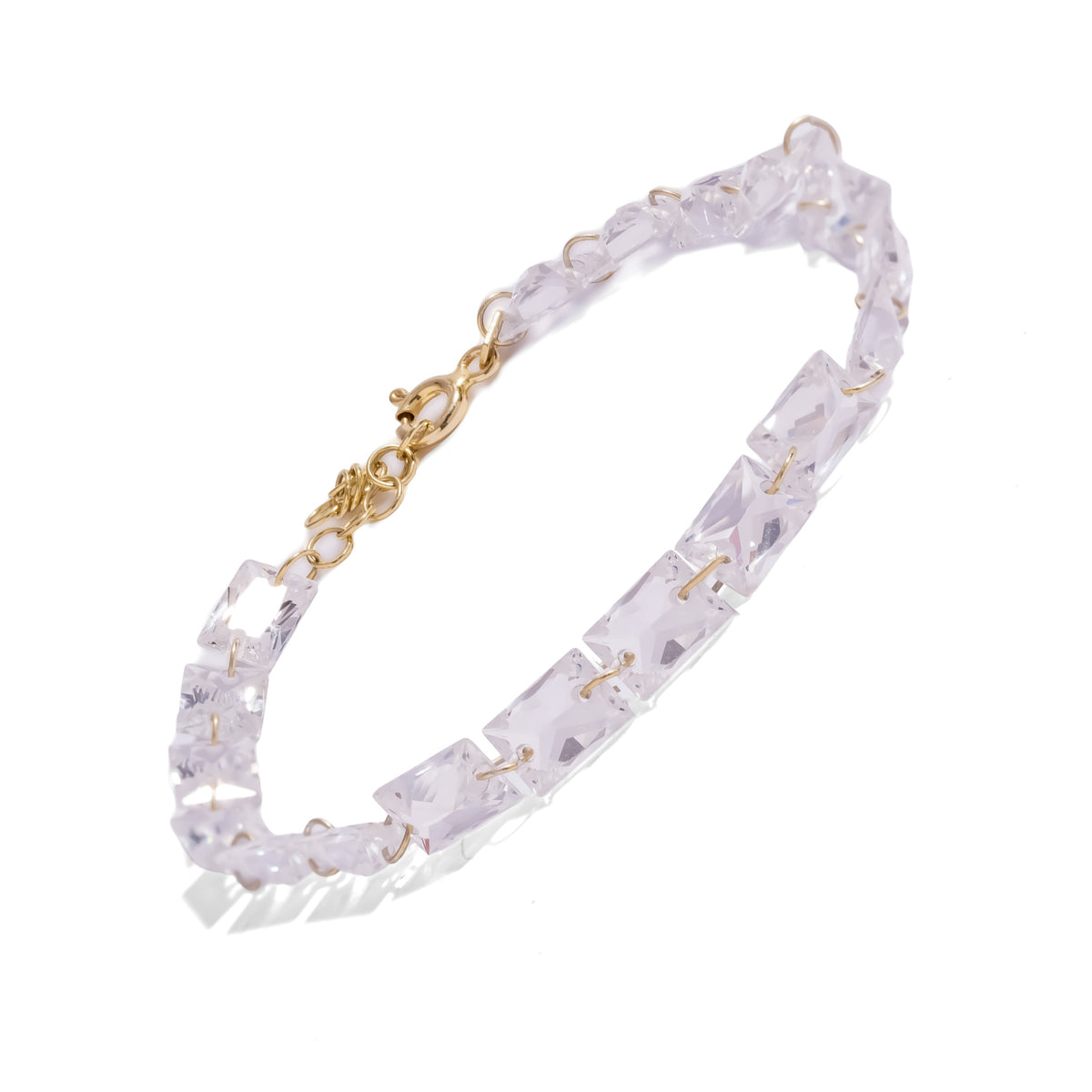 Starlight emerald cut zircon tennis bracelet laid diagonally on white with its gold clasp