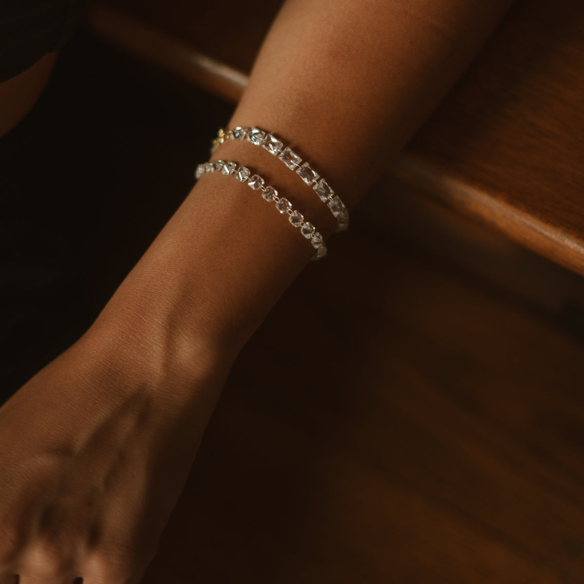 Starlight emerald cut tennis bracelet stacked with a trillion zircon bracelet on a wrist resting on a banister