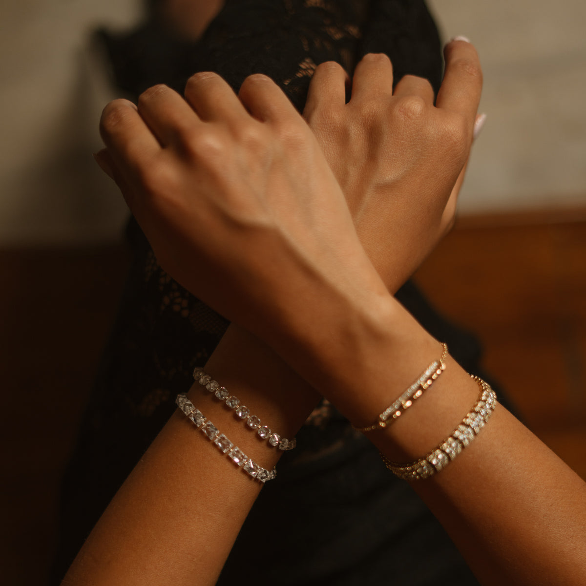 Crossed wrists showing the Starlight emerald cut zircon tennis bracelet with other gold bracelets