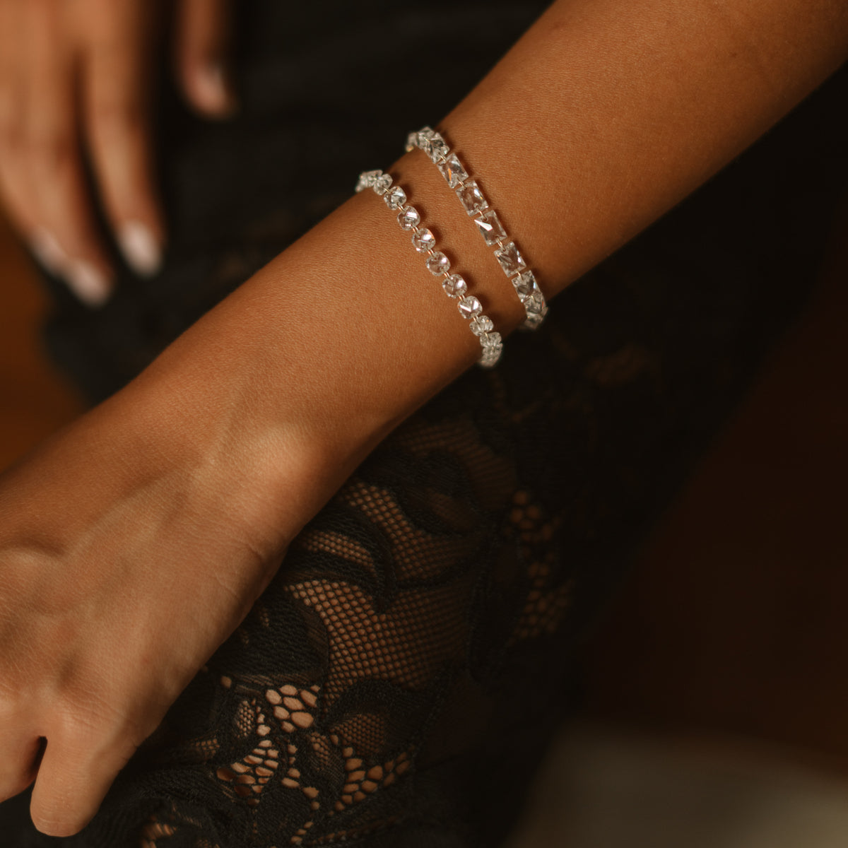 Close up of the Starlight emerald cut zircon tennis bracelet stacked on the wrist over black lace