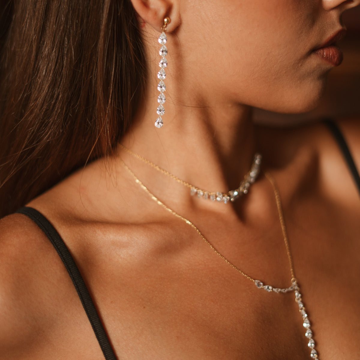 Close up of a Starlight Pear Cut Zircon Gold Drop Earring with layered zircon necklaces