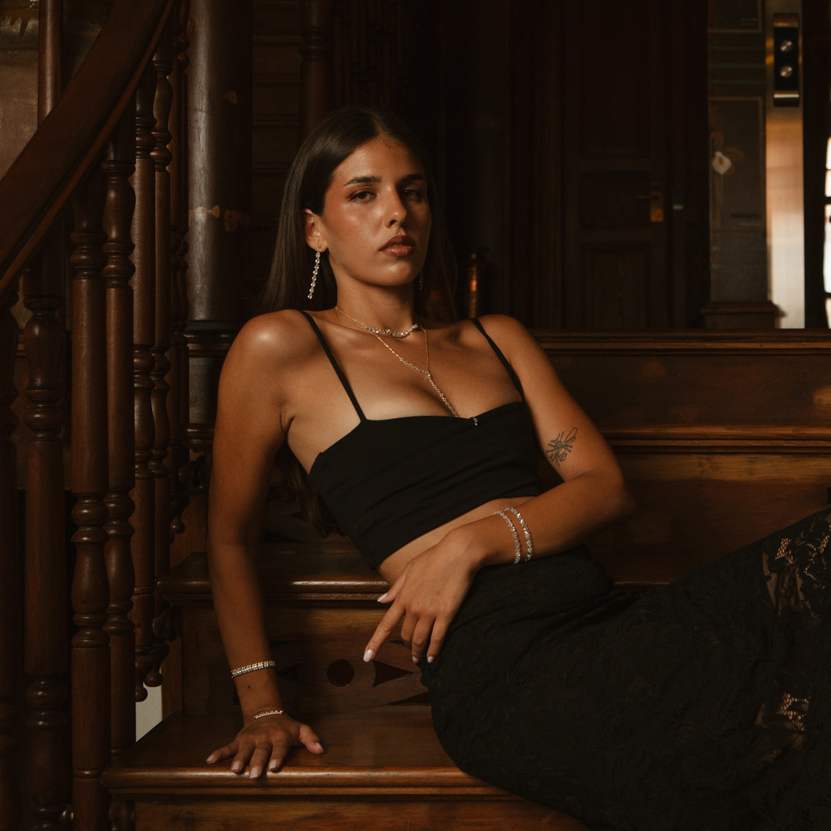 Model seated on a wooden staircase wearing the Starlight Pear Cut Zircon Gold Drop Earrings