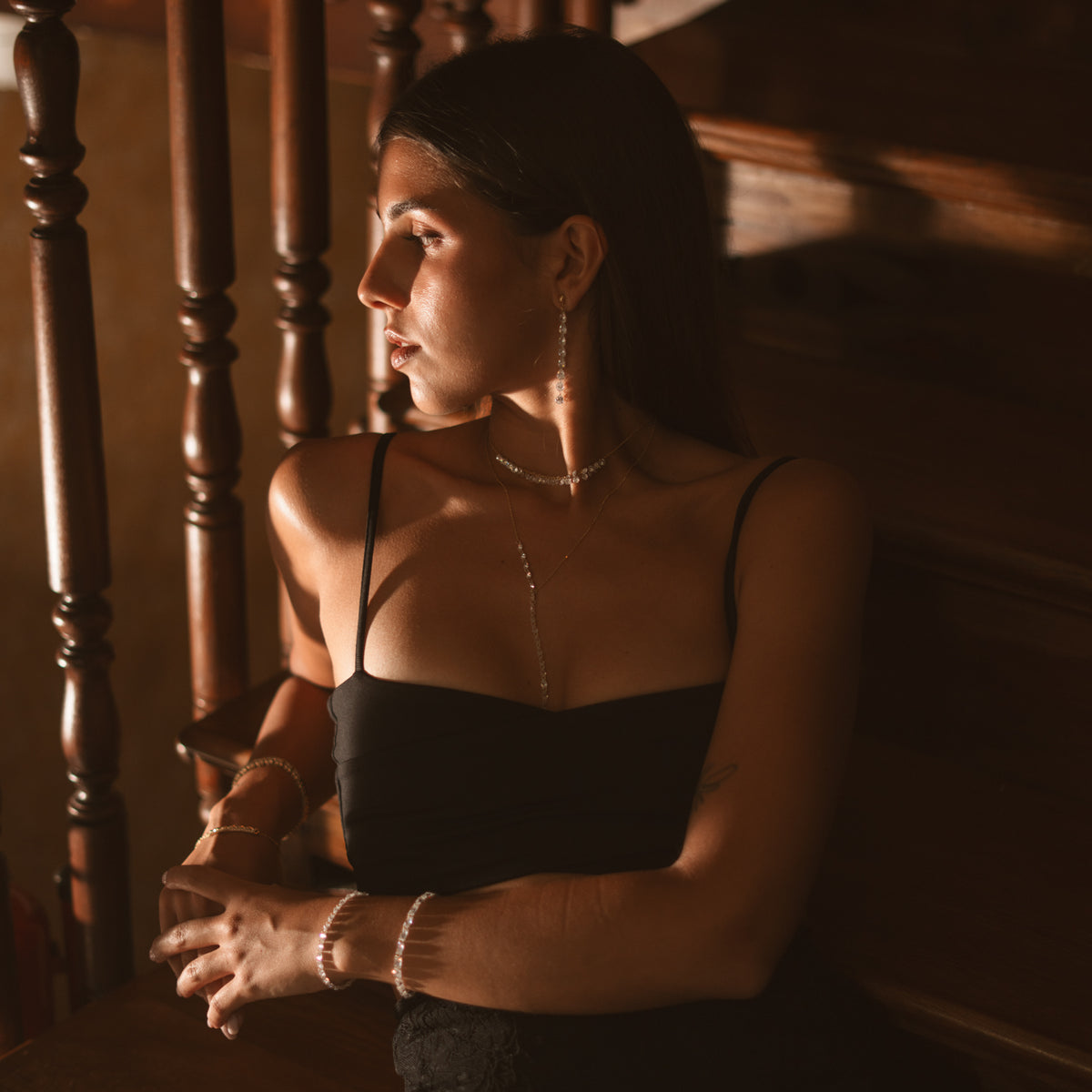 Model by a wooden banister wearing the Starlight trillion zircon tennis bracelet with Starlight earrings and necklaces