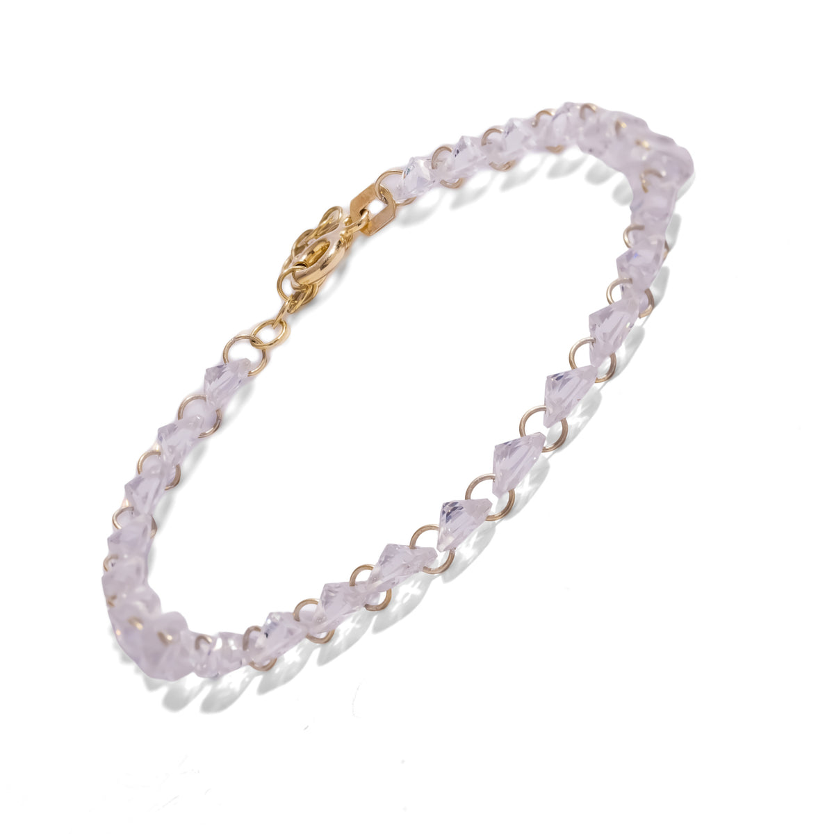 Starlight trillion zircon tennis bracelet laid diagonally on white with its gold clasp