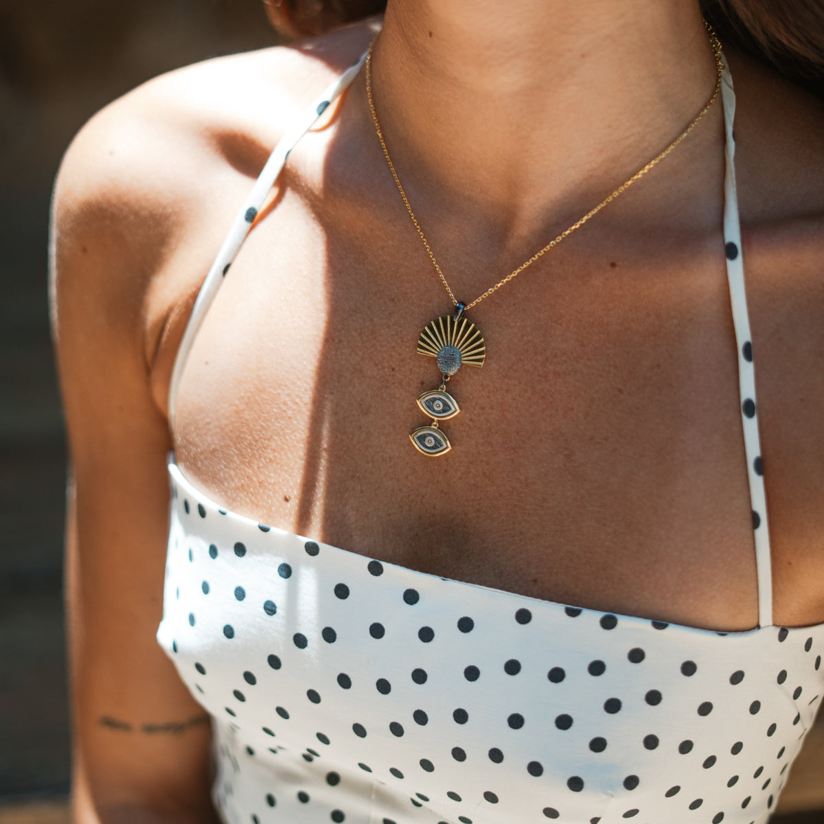 Detail of the Cleopatra Sun &amp; Watchful Eye Gold Statement Necklace on the neckline, gold sunburst fan above two oxidized silver evil eye drops