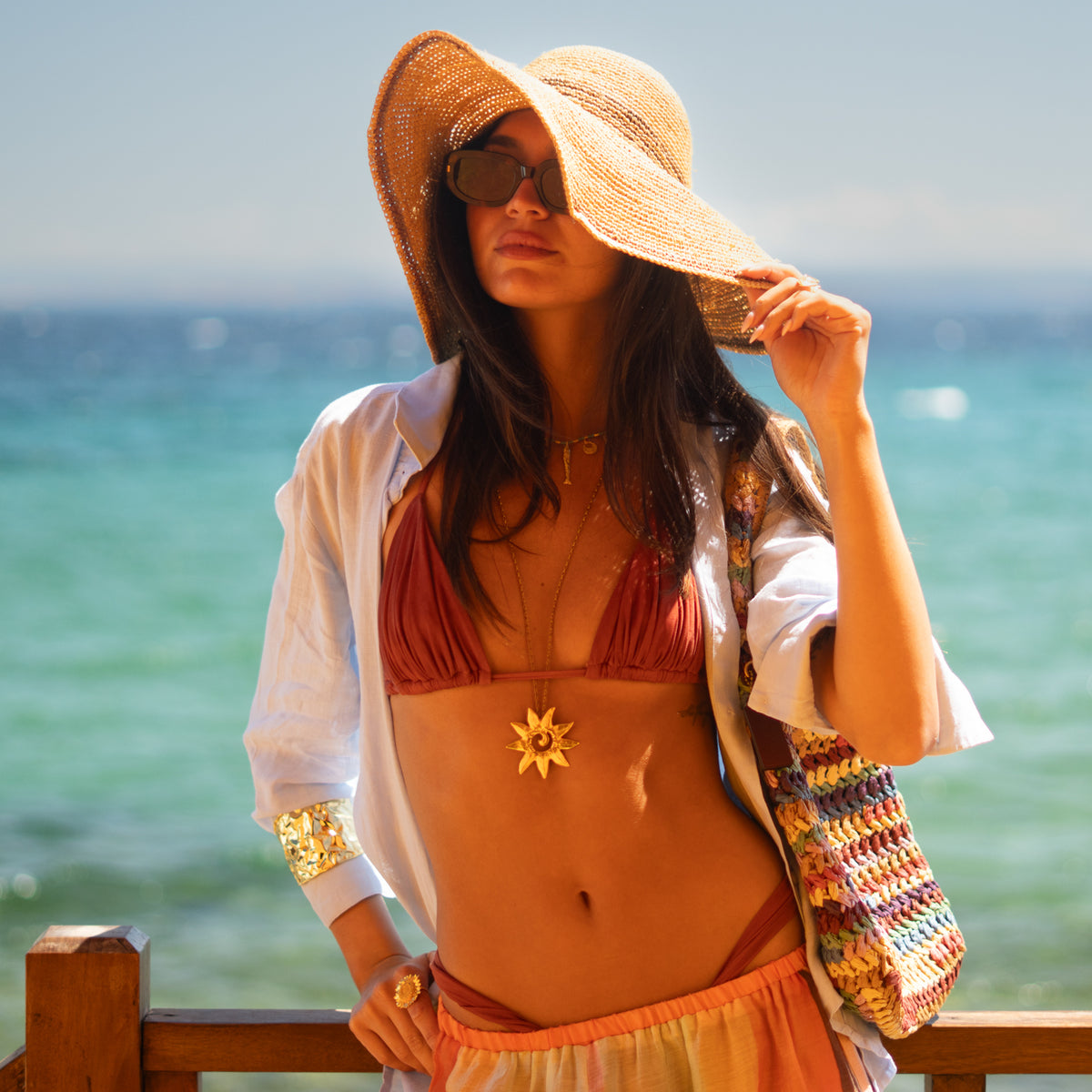 Gold sunburst pendant necklace styled with summer beach layers by the sea