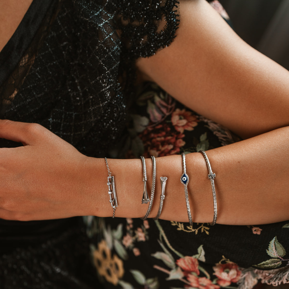 Forearm across a black lace dress, the Three Lights zircon bar bracelet leading a stack of silver bangles