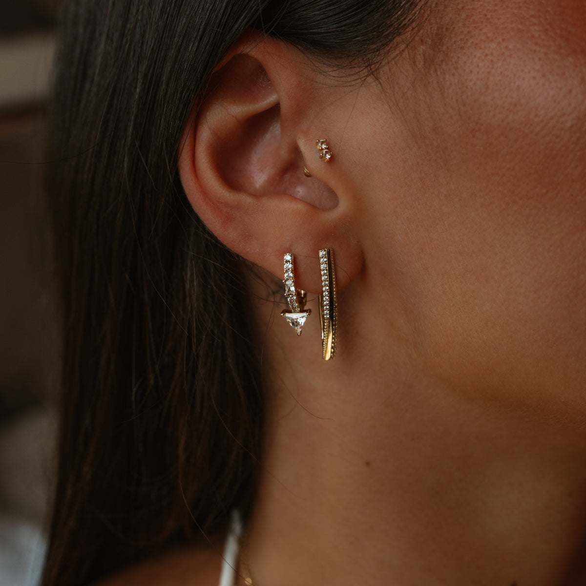 Close up of the Trillion Arrow Pave Zircon Gold Stud Earring worn in the lobe beside the Twisted Double Row Zircon Gold Hoop Earring