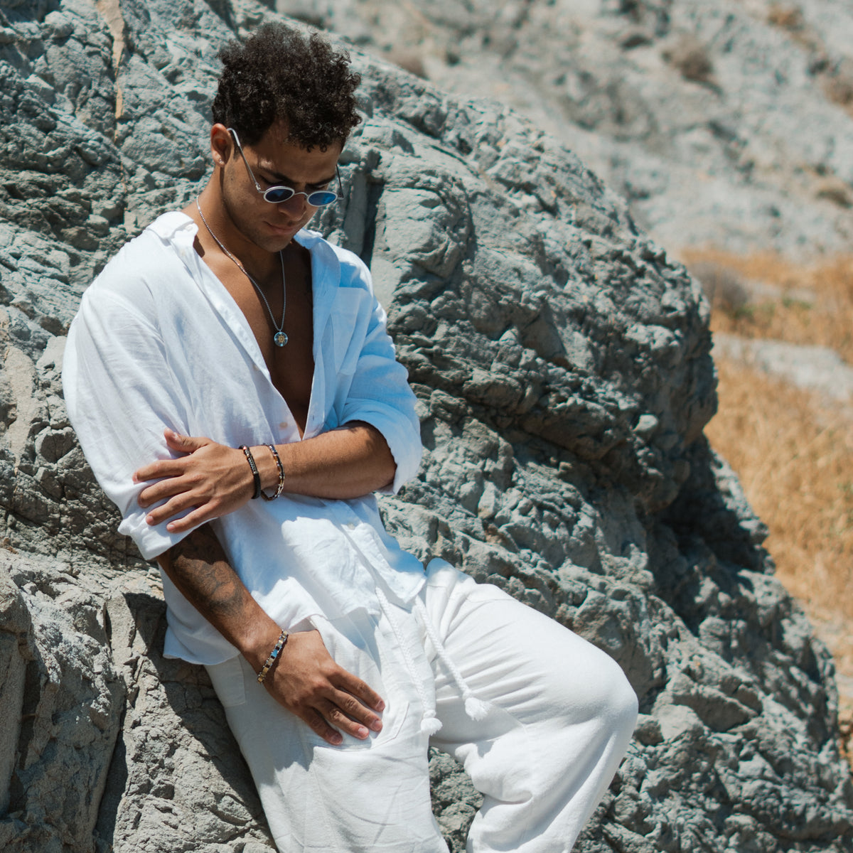 Man seated on rocks by the sea wearing the black and gold steel compass pendant necklace