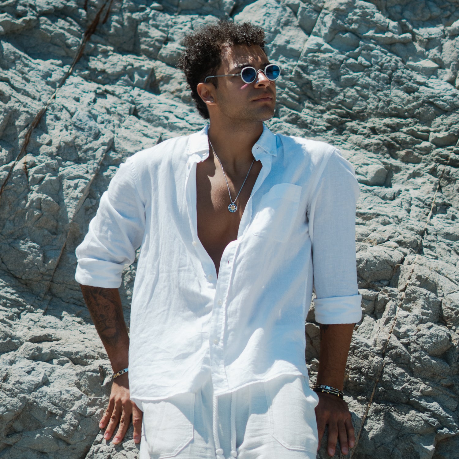 Man on the rocks in a white linen shirt wearing the True North compass ship wheel necklace