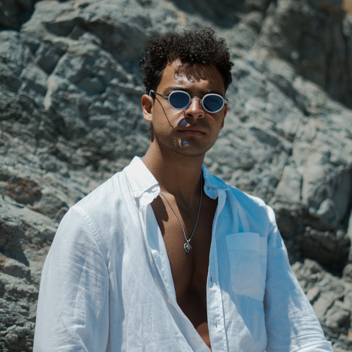 Man in sunglasses and a white linen shirt wearing the mens compass ship wheel necklace