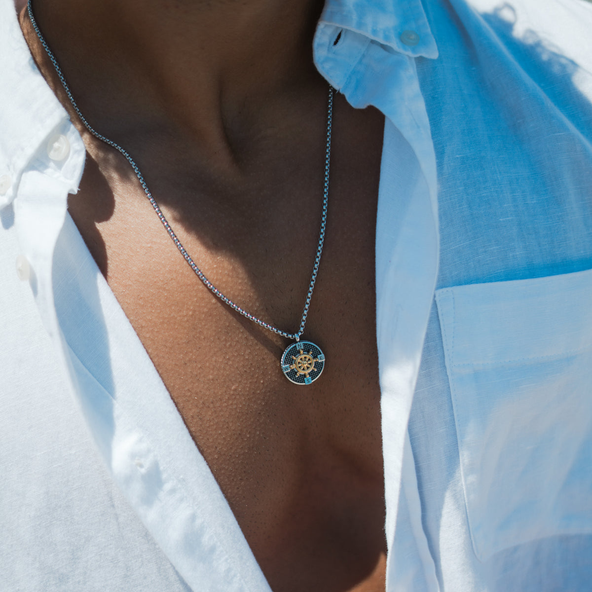 Close up of the black and gold compass ship wheel pendant worn with a white linen shirt