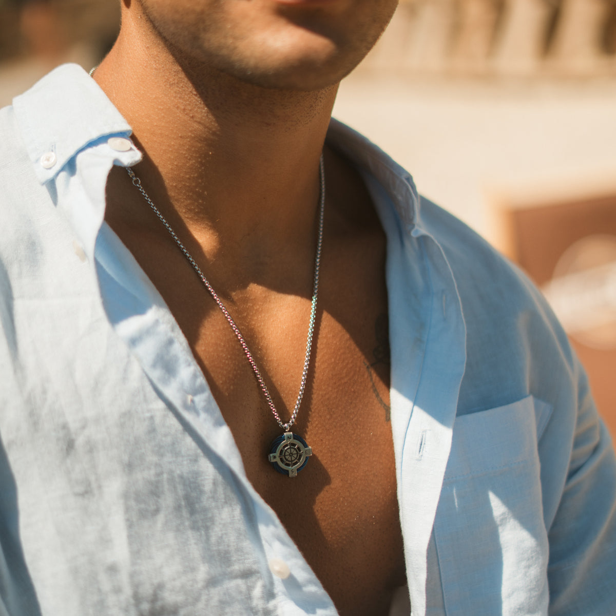 Steel compass ship wheel pendant resting mid chest over an open linen shirt