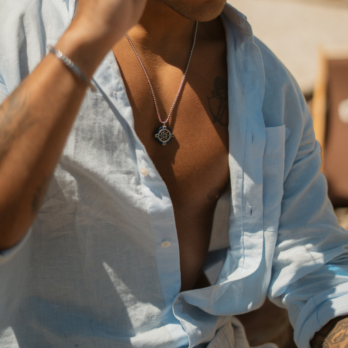 Man wearing the mens compass ship wheel necklace with a light linen shirt by the sea