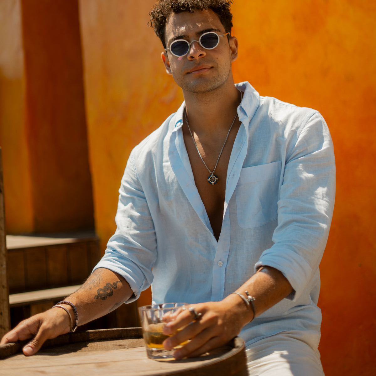 Man in sunglasses and a linen shirt wearing the steel compass ship wheel pendant necklace