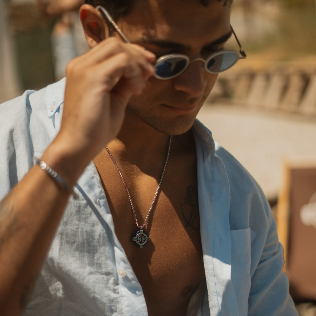 Man in a light blue linen shirt wearing the True North compass ship wheel steel necklace