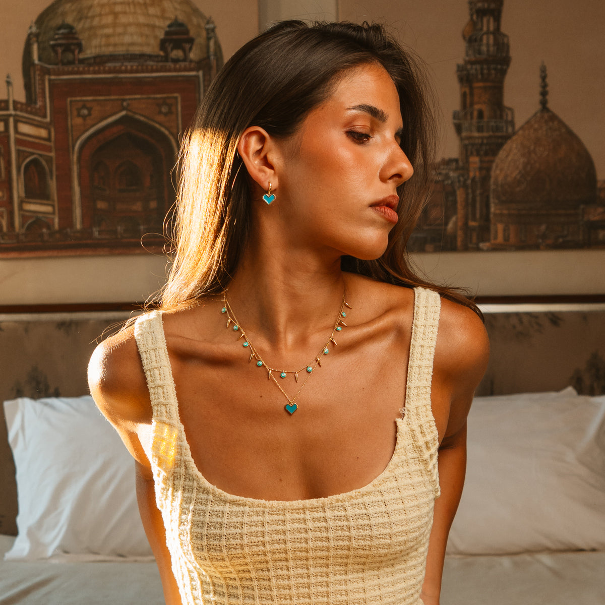 Model looking away wearing the Turquoise Evil Eye & Gold Spike Charm Necklace with turquoise heart earrings and pendant