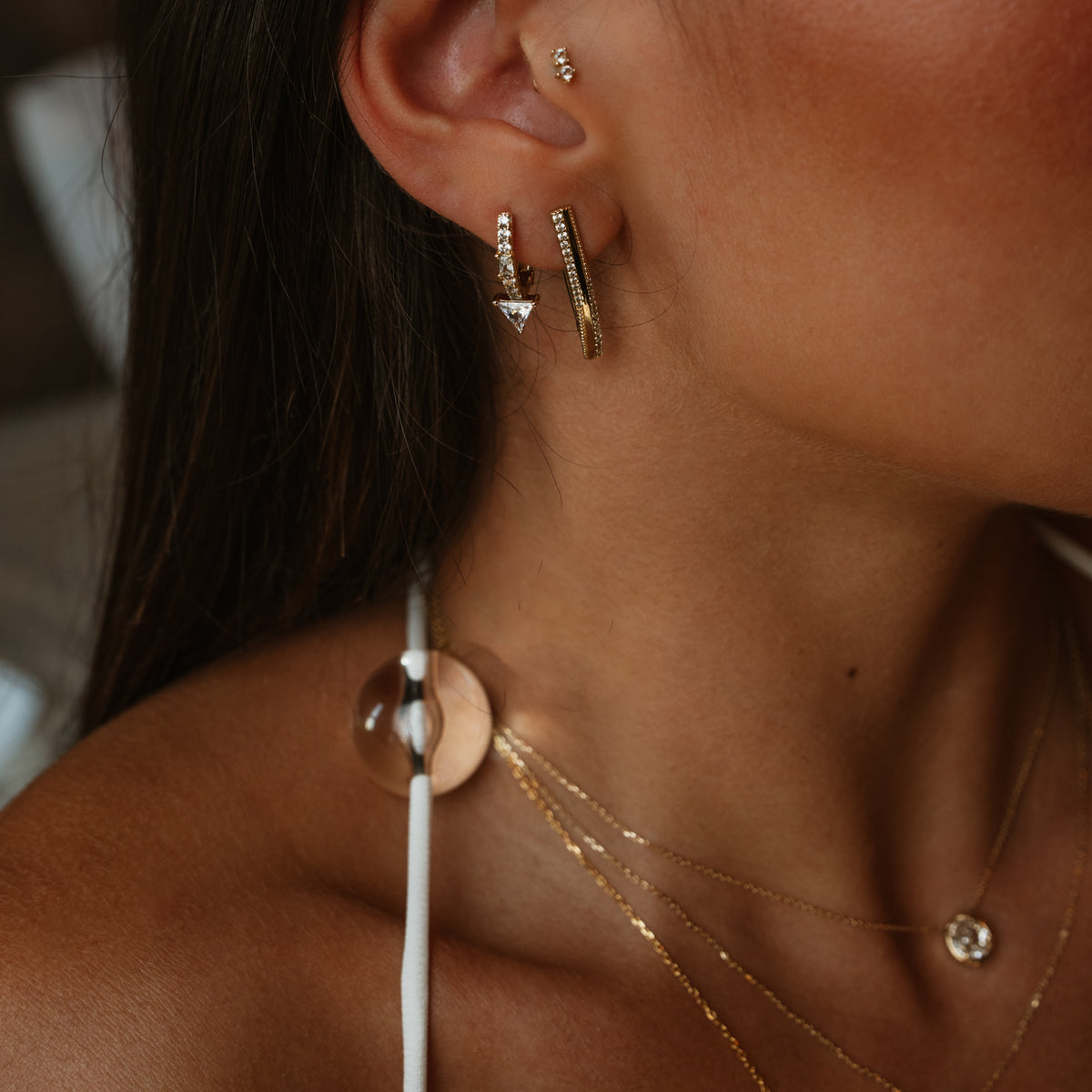 Side view of the ear wearing the twisted double row gold hoop earring with layered gold necklaces