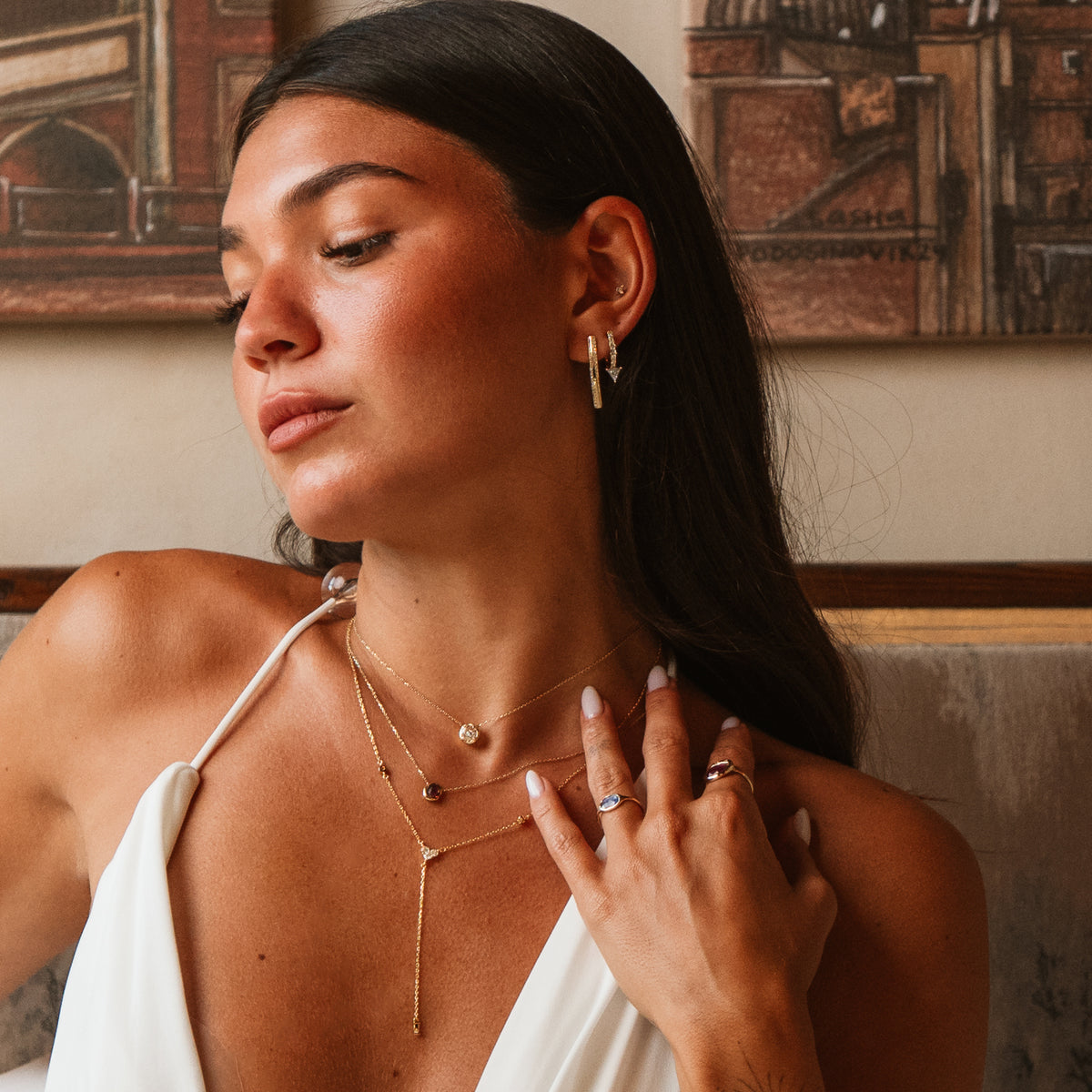 Model in a white halter top wearing the twisted double row gold hoop earrings with layered gold necklaces