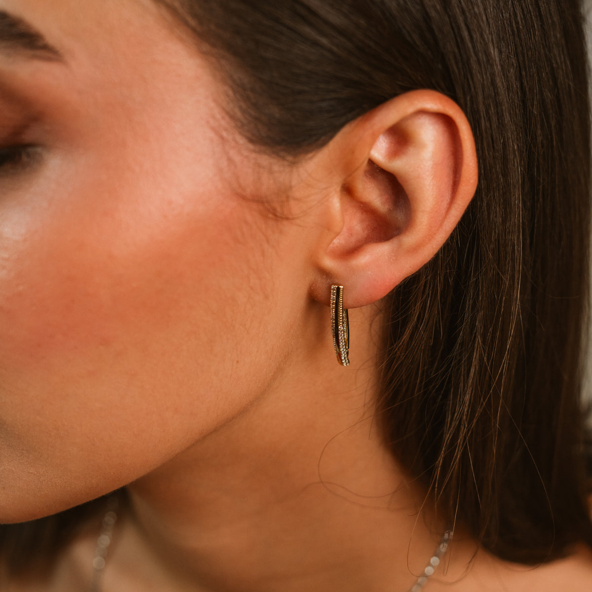 Close up of a twisted double row zircon gold hoop earring on the ear
