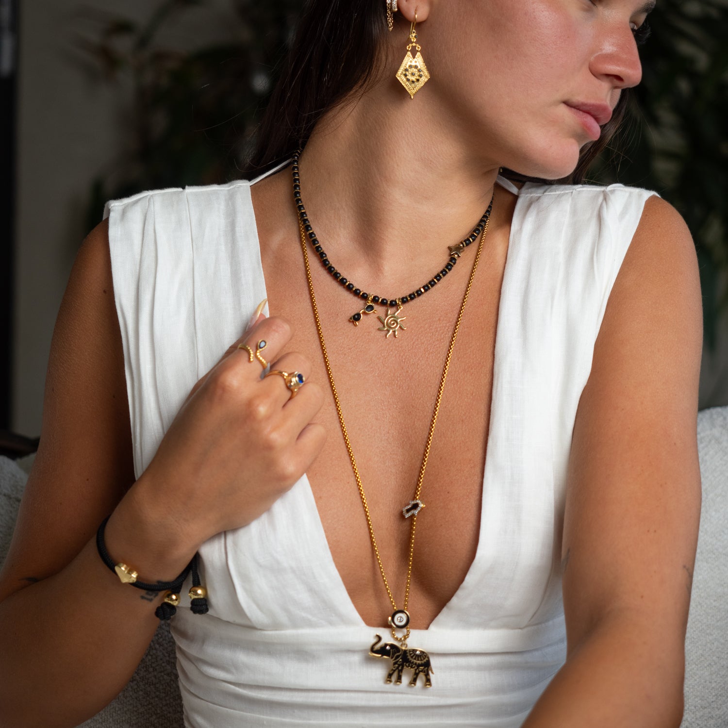 Model wearing black onyx beaded sun necklace layered with gold chain, styled with white linen dress