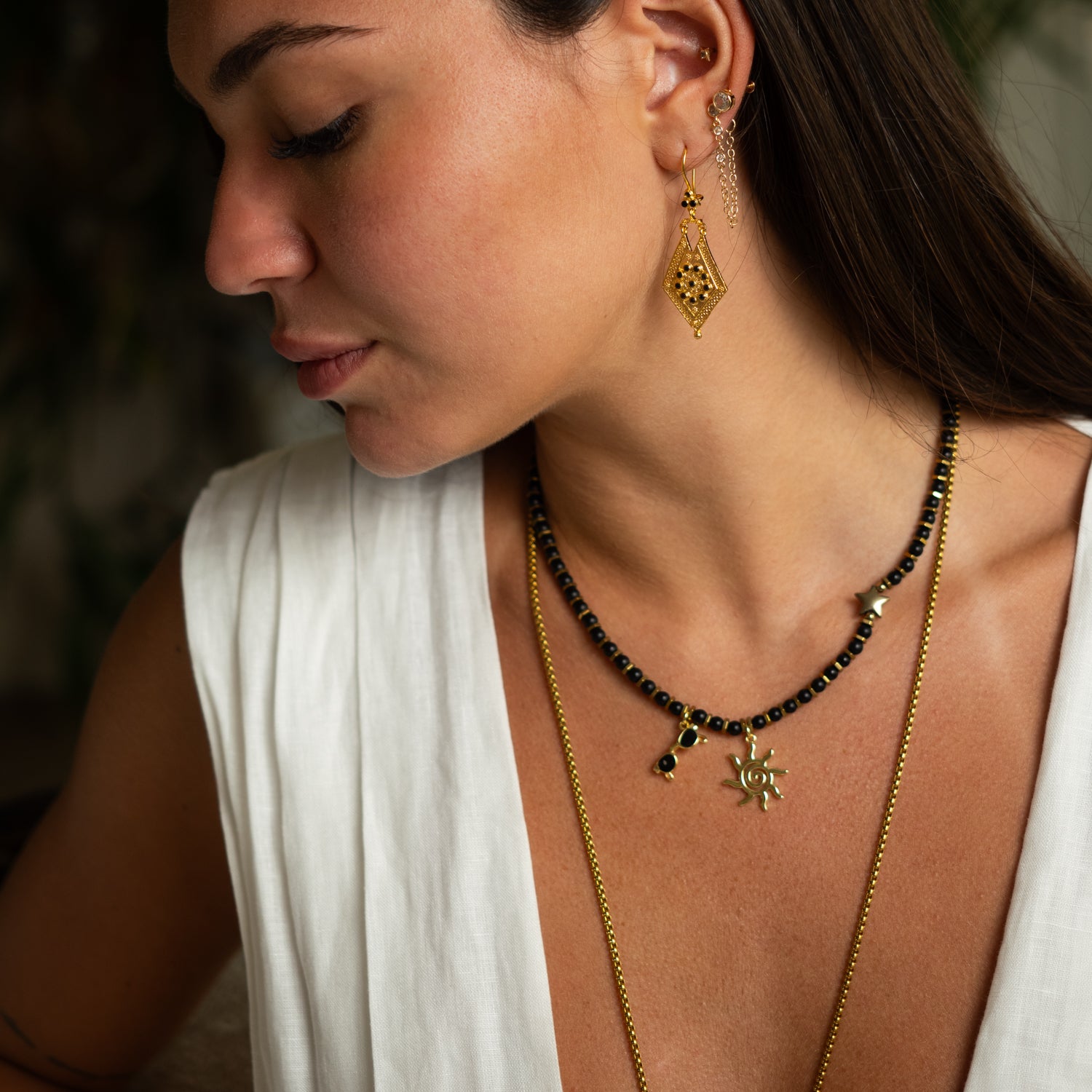 Close-up of 18k gold-plated sun pendant and sunglasses charm on black onyx beaded necklace