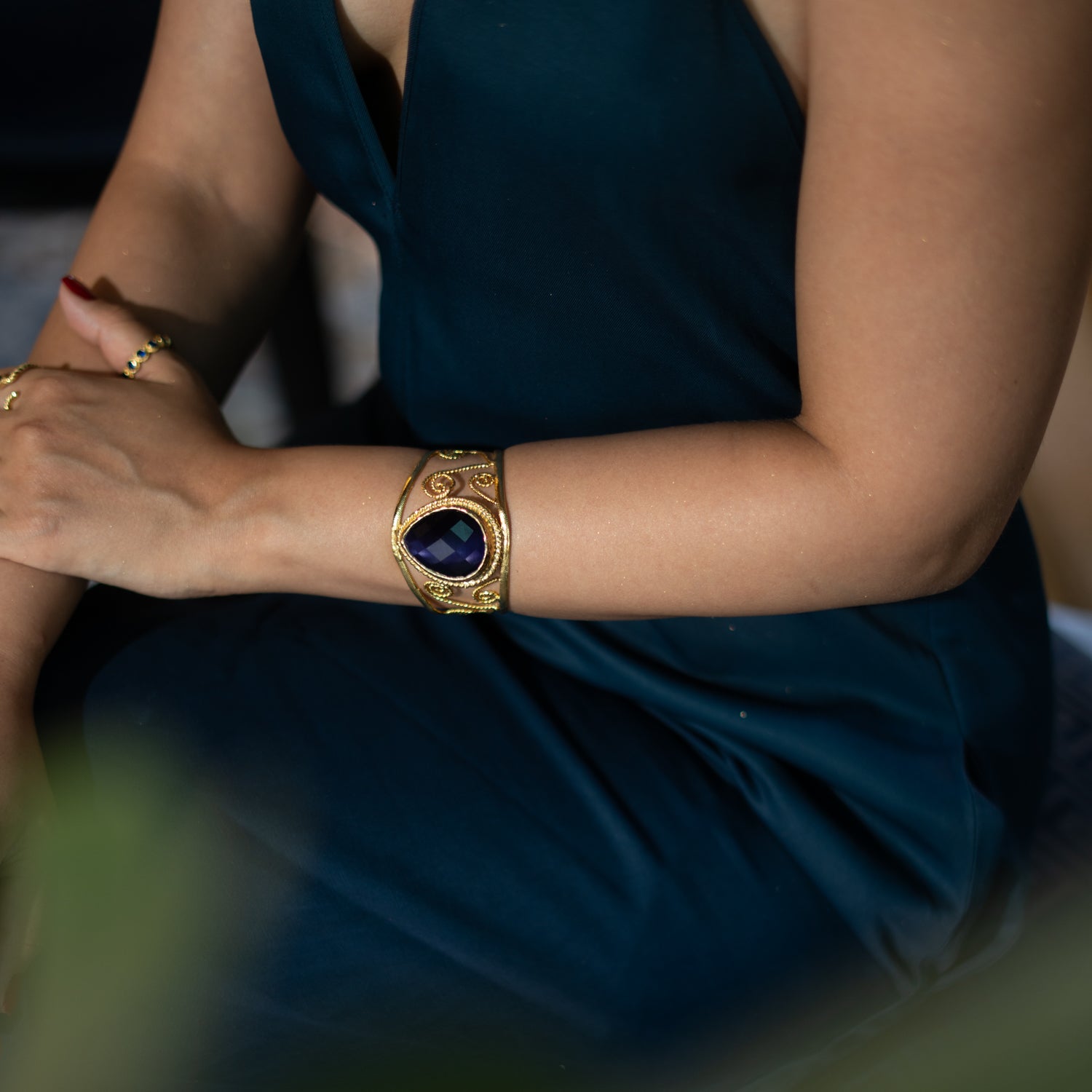 Chunky cuff bracelet in 24k gold-plated bronze featuring a navy blue cat eye stone and ornate gold swirl accents, vintage inspired design