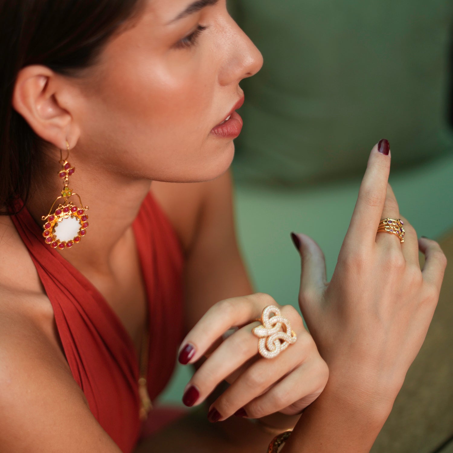 Artistic vintage-style earrings featuring a large mother of pearl stone surrounded by ruby and jade gemstones, set in chunky gold for a unique look.
