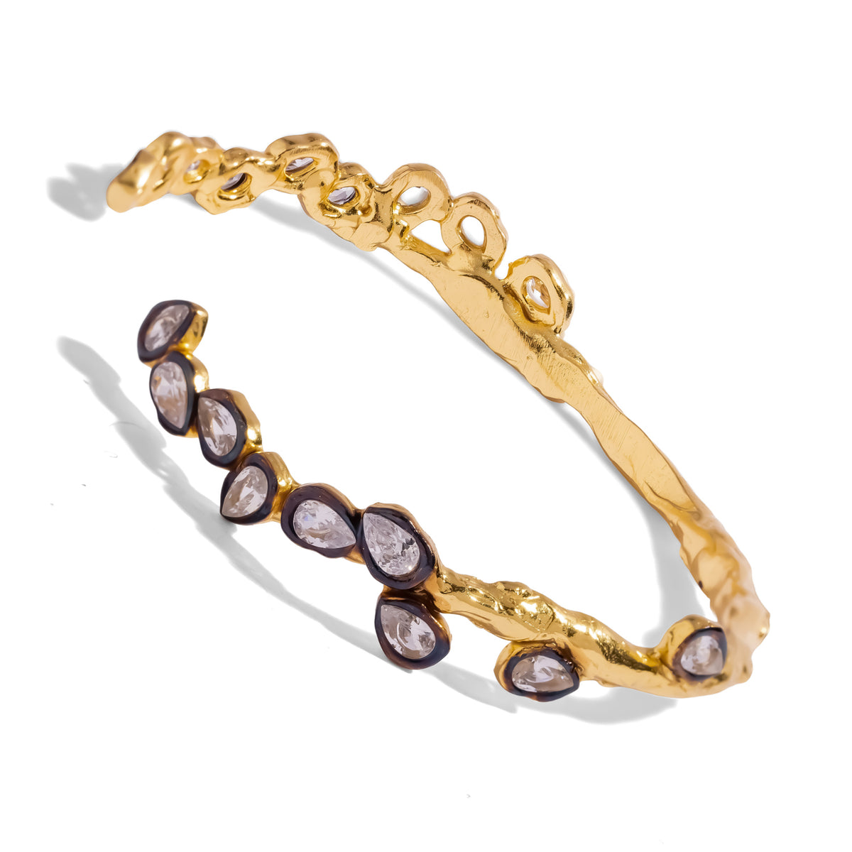 Open gold cuff with a row of white cubic zirconia teardrops in blackened bezels, angled view