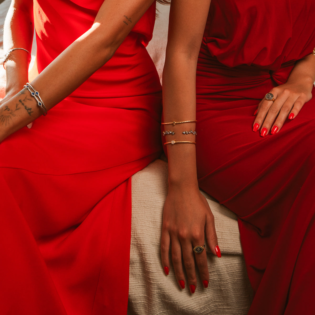 Two models in red dresses, one wearing the vintage style teardrop gold cuff in a stack of slim gold bracelets