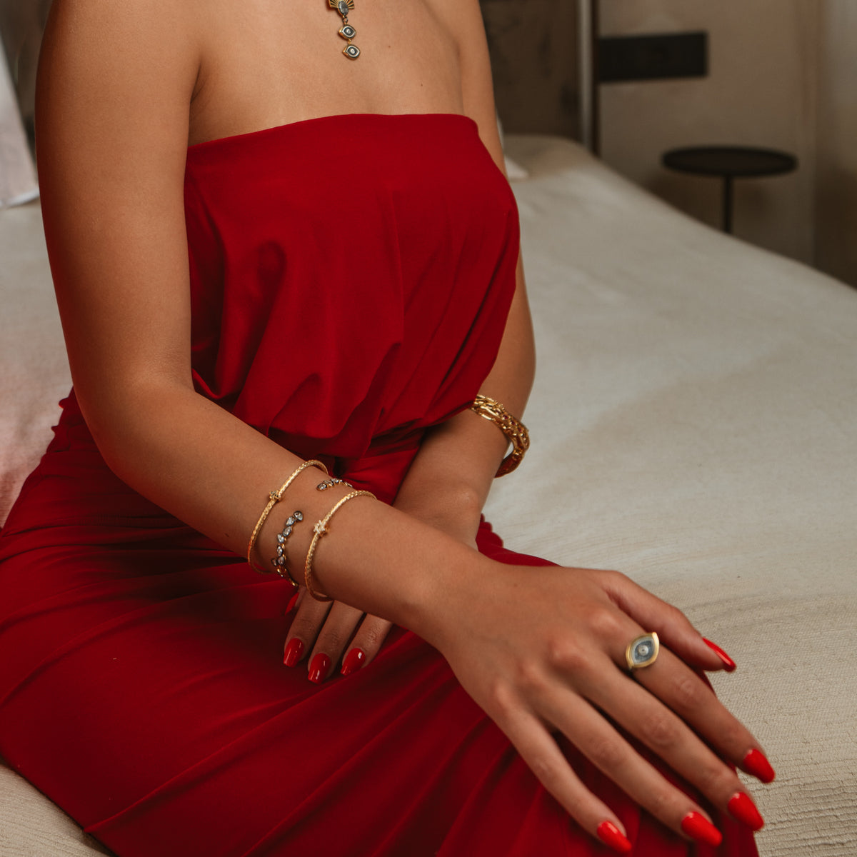 Model in a strapless red dress wearing the teardrop gold cuff with stacked gold bracelets and an evil eye ring