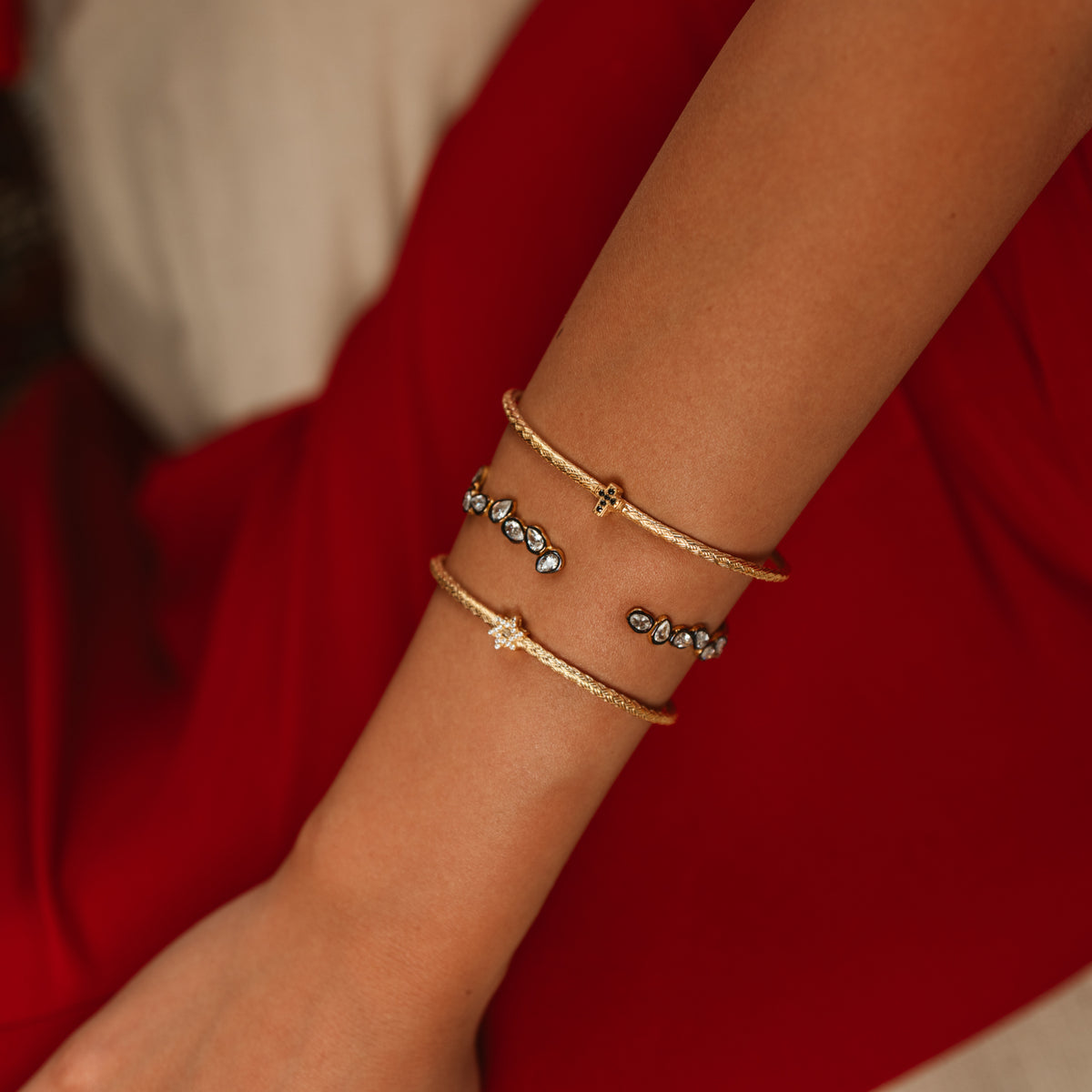 Teardrop two tone gold cuff stacked between two slim gold cuffs on a wrist against a red dress