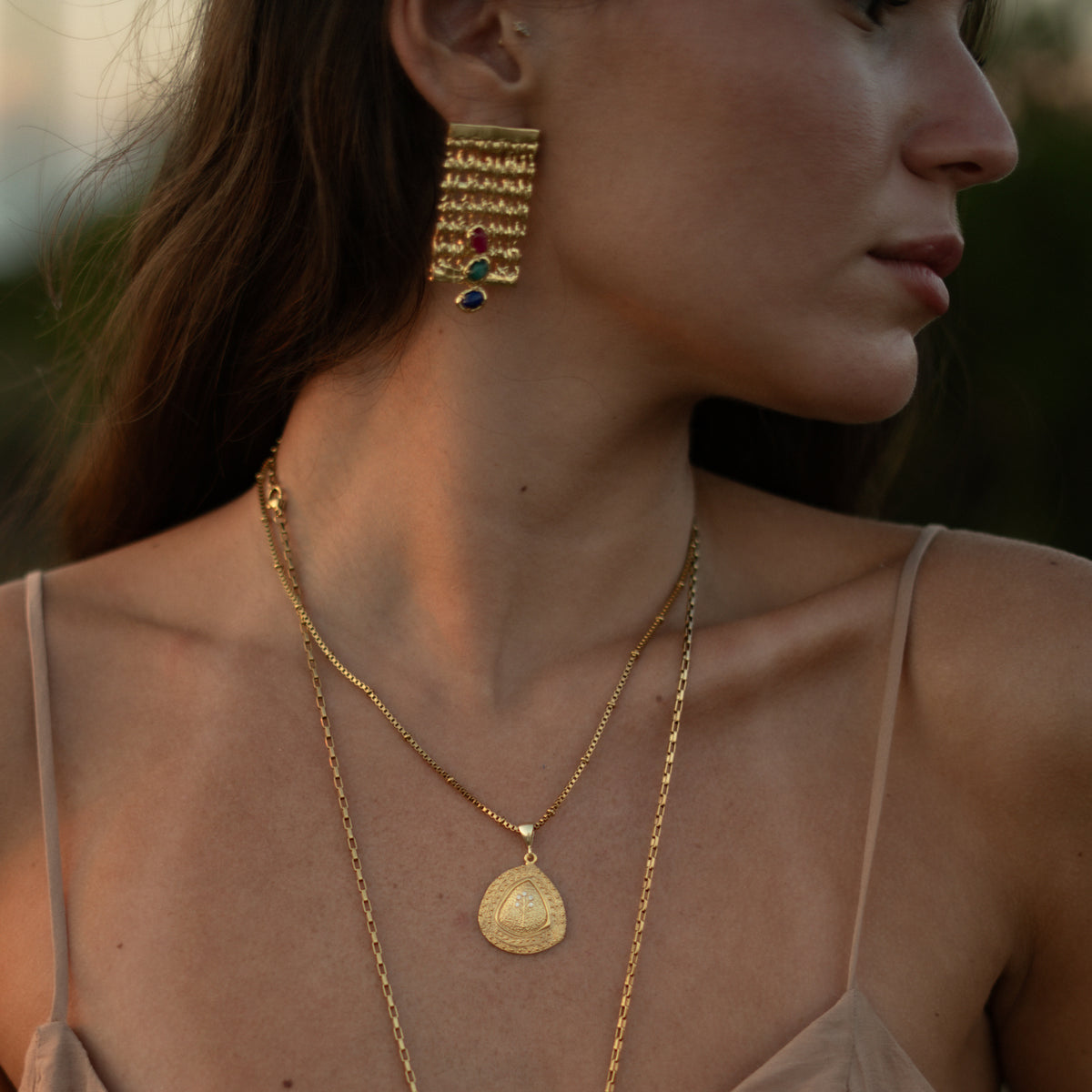 Side profile of a woman wearing the Tree of Life gold pendant necklace with fringed gold statement earrings