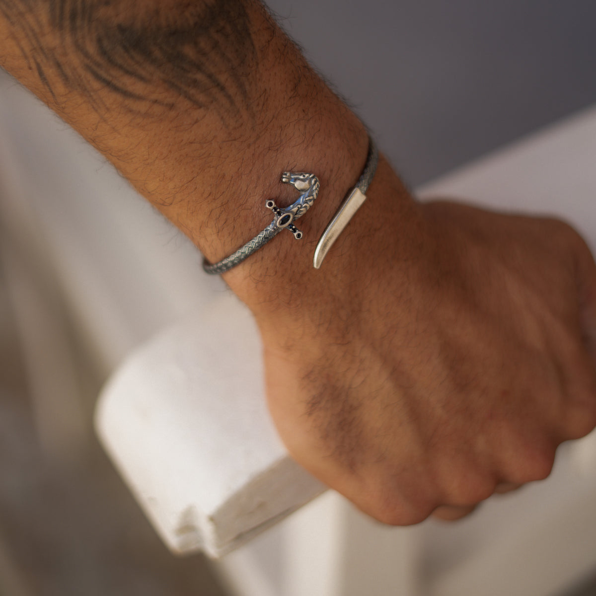 Man's wrist wearing the oxidized sterling silver saber wrap bracelet, hand resting on a white railing