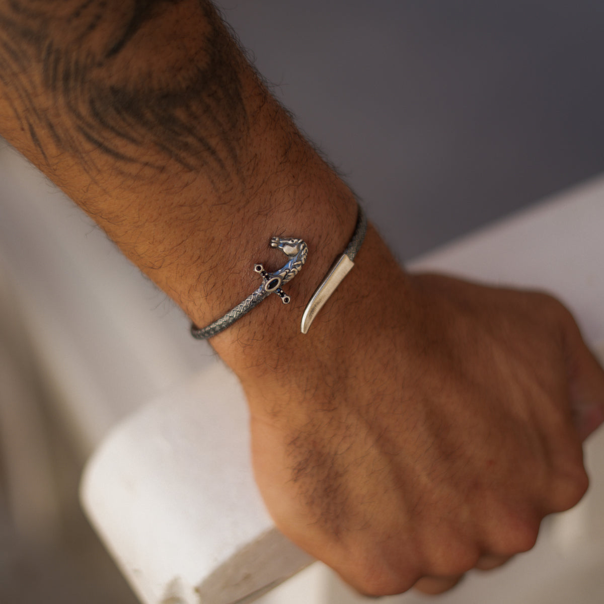 Close view of the horse saber wrap bracelet worn on a man's wrist, the black zircons on the cross guard catching the light