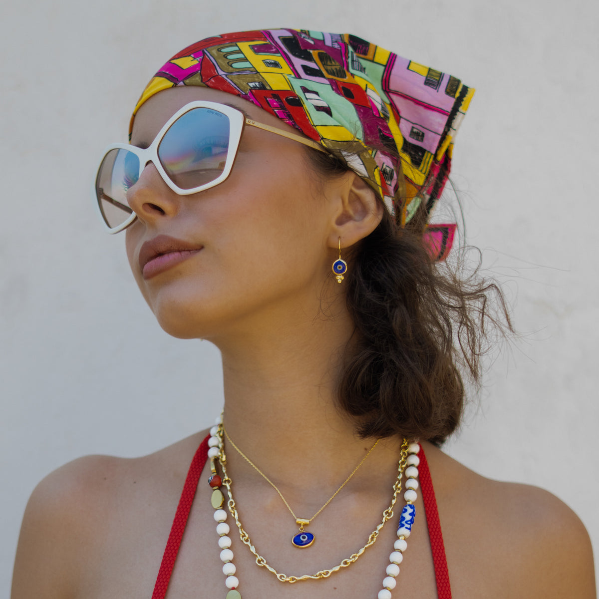 Model in a printed headscarf wearing the Watch Over Me blue evil eye earrings and matching necklace