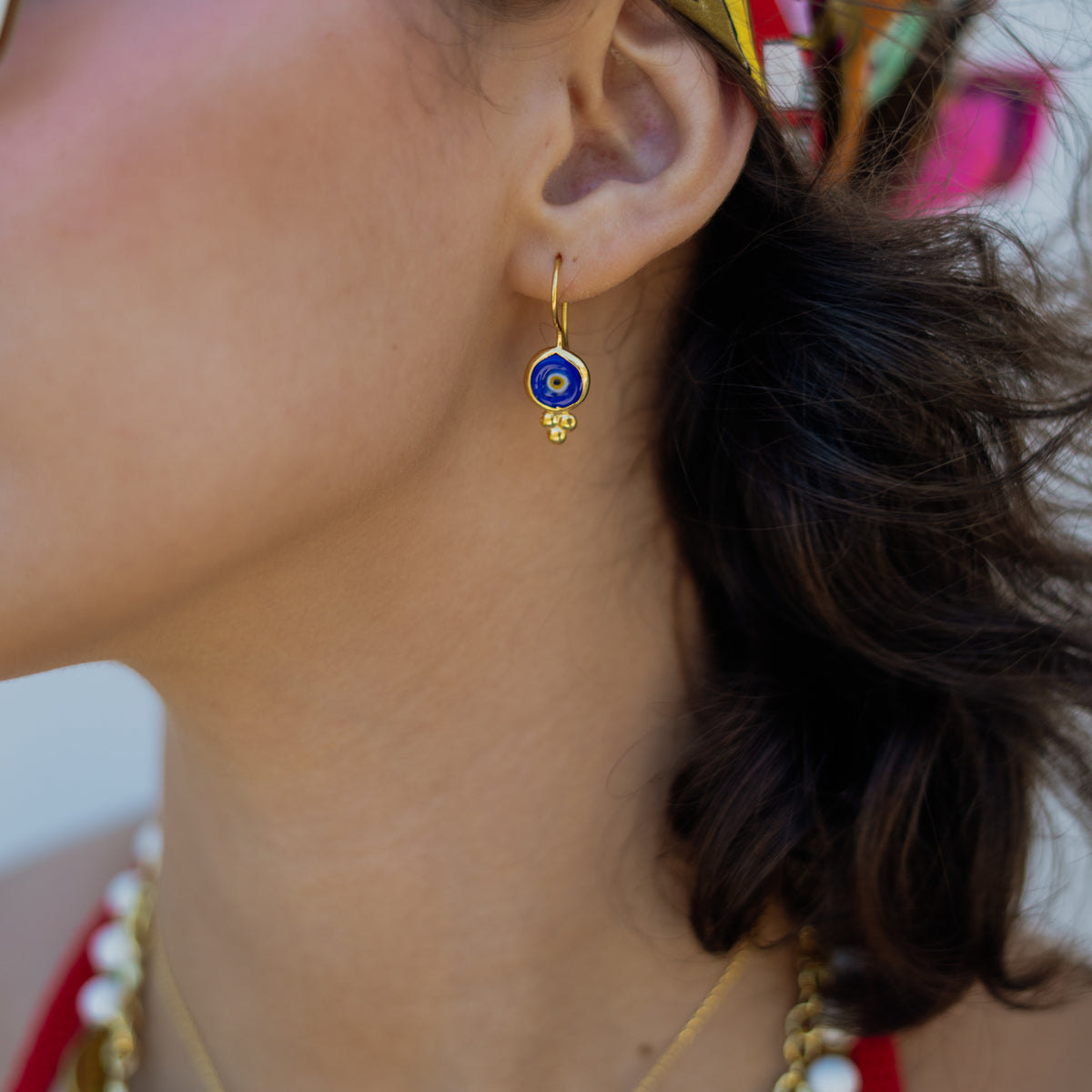 Close up of a Watch Over Me blue evil eye gold drop earring on the ear